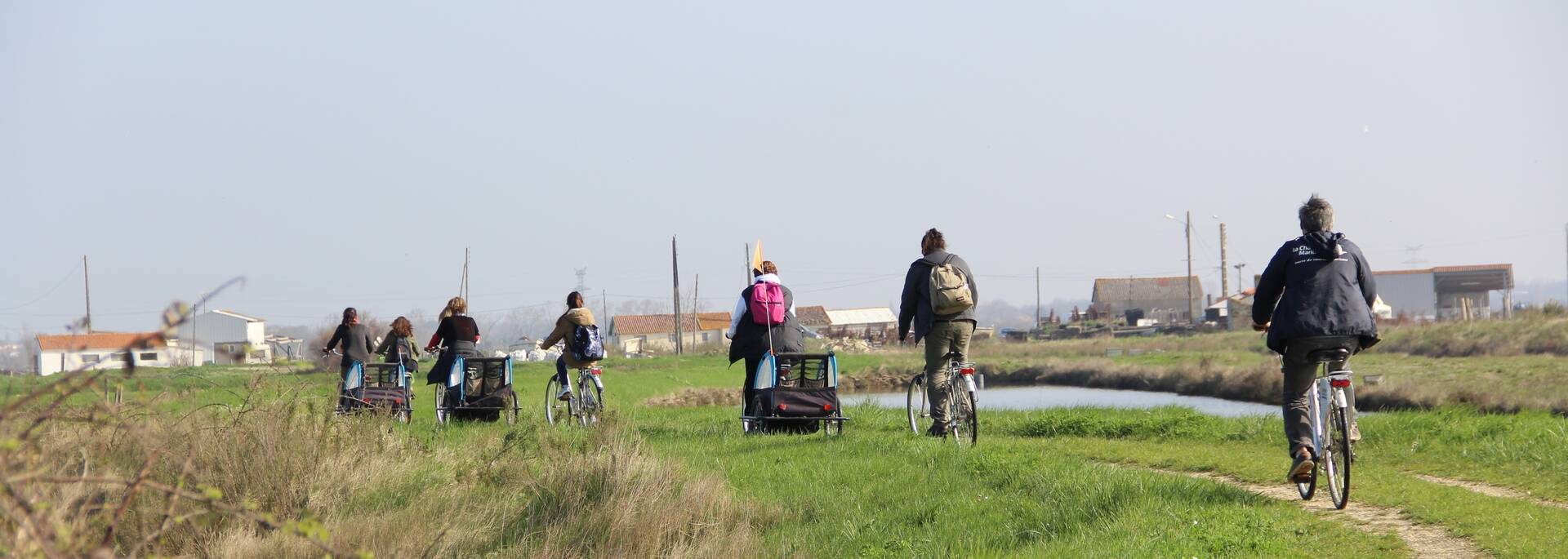 Un groupe fait du vélo suyr un chemin à travers les marais pour visiter la cité des huitres.
