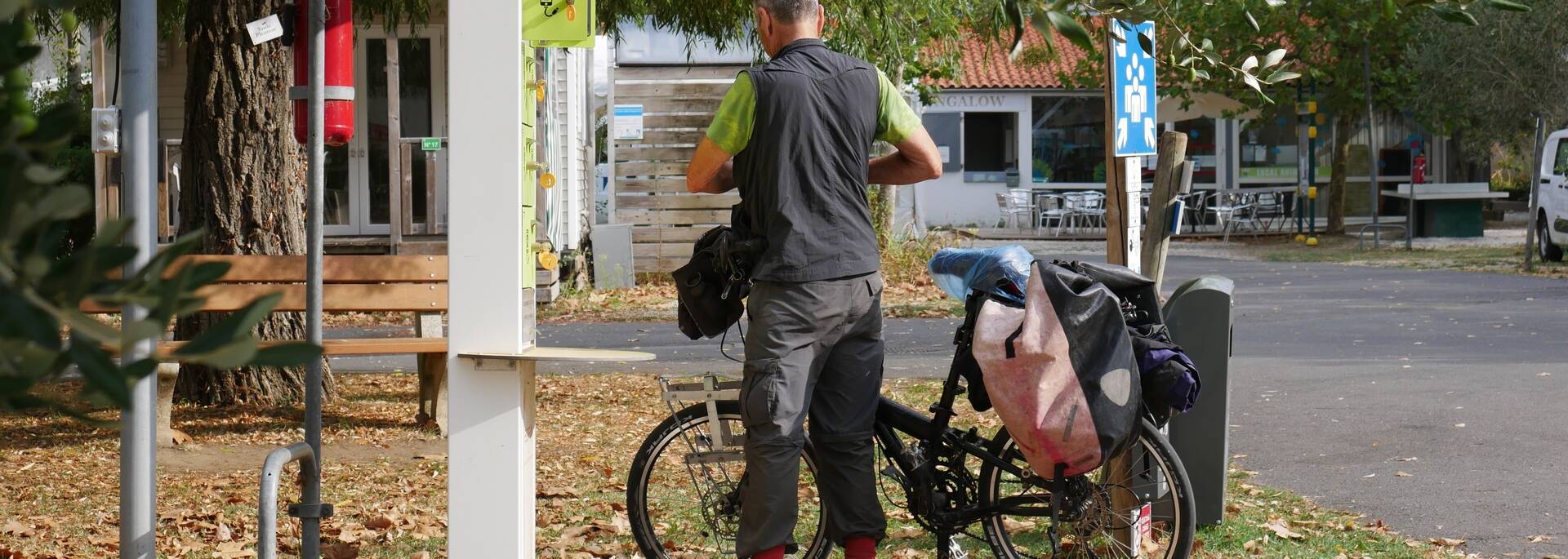 Un monsieur range ses affaires devant son vélo. il transporte des sacs sur son porte bagages et à l'aire de faire une pose sur son long trajet.